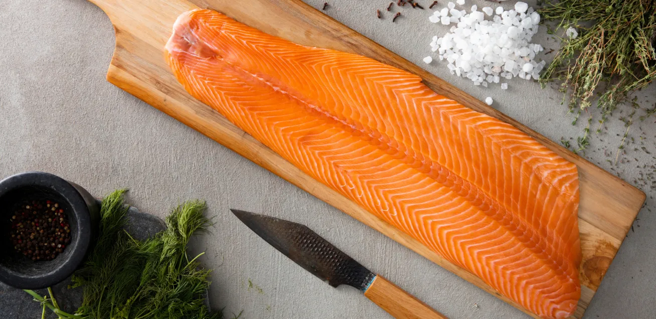 Filete de salmón sobre tabla de madera con cuchillo y especias